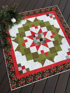 a green and red quilted table topper on a wooden floor next to a christmas tree