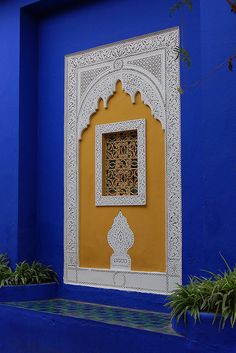 a blue and yellow wall with a window in the middle, surrounded by potted plants