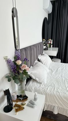 a white bed sitting next to a table with flowers in a vase on top of it