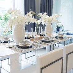 a dining room table with white flowers in vases and place settings on the plates