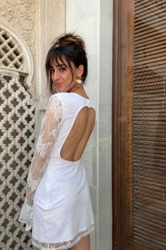 a woman standing in front of a door wearing a white dress with lace on it