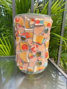 a colorful vase sitting on top of a table next to some green plants and trees