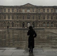 a person standing in front of a building on a rainy day with an umbrella over their head