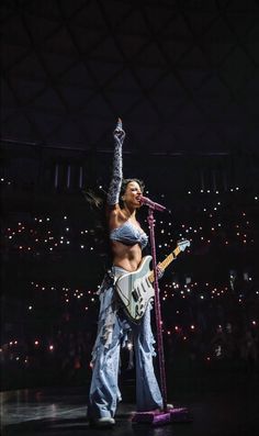 a woman standing on top of a stage with a guitar in her hand and holding a microphone