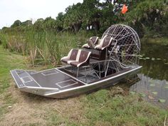 a boat that is sitting in the grass next to some water and trees with an animal cage on top