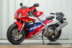 a red, white and blue motorcycle parked in front of a metal wall on a wooden floor