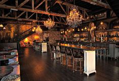 an empty bar with chandeliers hanging from the ceiling and wooden flooring in front of it