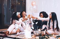 three women sitting on the floor toasting with wine glasses in front of balloons and confetti