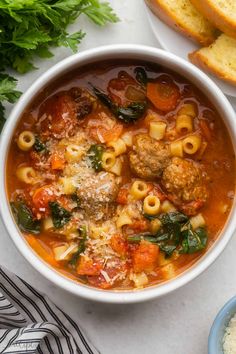 a bowl of pasta soup with meatballs, spinach and parmesan bread