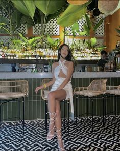 a woman sitting on top of a chair in front of a bar with plants behind her