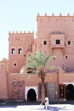 a large building with a palm tree in front of it and two people walking by