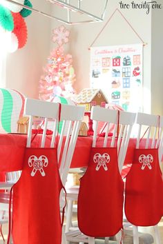 red aprons are hanging from the back of white chairs in front of a christmas tree