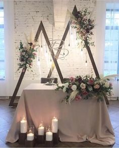 a table with candles and flowers on it in front of a white brick wall,