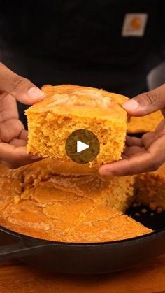 two hands holding a piece of cornbread in a skillet on a wooden table