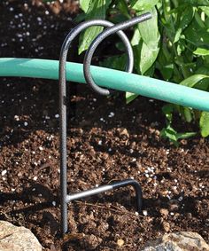 a garden hose is attached to a metal stand in the ground with dirt and rocks around it