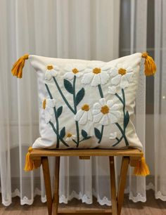 a white pillow with yellow tassels sitting on a wooden chair in front of a window