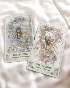 two tarot cards with pictures of bees on them sitting on a white bed sheet