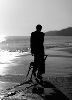 a man standing on top of a beach next to the ocean with a bike in front of him