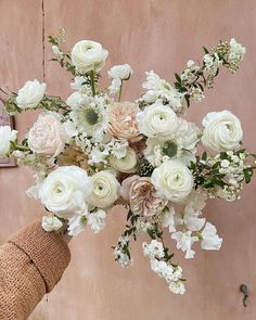 a vase filled with white and pink flowers on top of a wooden table next to a wall