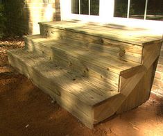 a wooden porch with steps leading up to the front door and side window in the background