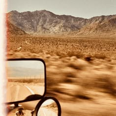 the view from a car's side mirror on a desert road with mountains in the background