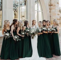 a group of women standing next to each other in front of a building holding bouquets