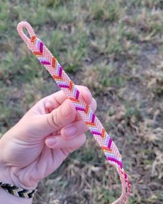 a hand holding a pink, yellow and purple braided bracelet in the middle of grass