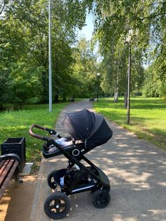 a stroller sitting on the side of a road next to a park bench and trees