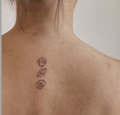 the back of a woman's neck with three seashells on it