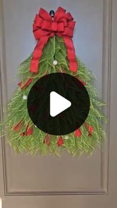 a christmas wreath hanging on the front door with a red bow and green leaves around it