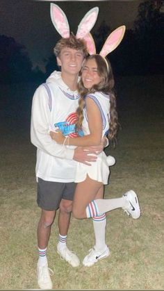 a man and woman dressed in bunny ears hugging each other on the grass at night