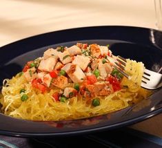 a black plate topped with pasta and chicken on top of a blue table cloth next to a fork