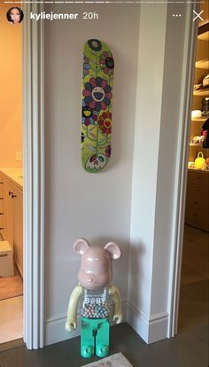 there is a toy bear sitting on the floor next to a skateboard hanging on the wall