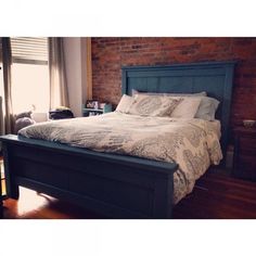 a large bed sitting next to a window in a room with wooden floors and brick walls