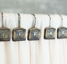 four metal hooks hang from the curtain in front of white drapes with texas longhorns on them