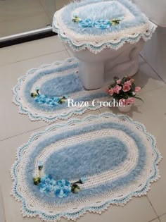 two crocheted rugs on the floor next to a toilet with blue flowers