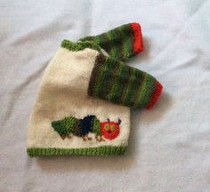 two knitted sweaters on top of a bed with white sheets and green trim