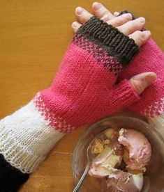 a child's hand wearing a pink and white knitted mitt next to a bowl of ice cream