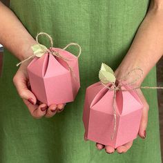 two hands holding pink paper boxes tied with twine