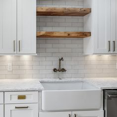 a kitchen with white cabinets and marble counter tops, an open shelving above the sink