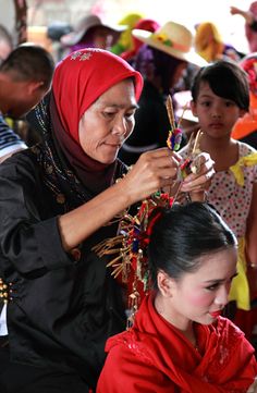 a woman is cutting another woman's hair in a crowded area with other people