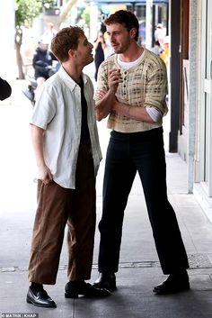 two men standing next to each other on the sidewalk talking and laughing together with one man wearing a white shirt and tie