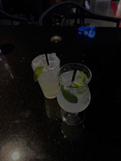 two glasses filled with drinks sitting on top of a black table next to each other