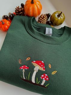 machine embroidered sweatshirt featuring a cute mushroom scene with falling leaves colours pictured are sand and forest green embroidered onto a gildan sweatshirt, composed of 50% cotton and 50% polyester sizing as follows Sizes: S (50,8cm-68,6cm) / M (55,9cm-71,1cm) / L (61cm-73,7cm) / XL (66cm-76,2cm) / XXL ( 71,1cm-78,7cm) these are made to order and i may need to order your preferred size & colour, so please allow time for your sweatshirt to be ready!  if you have any questions or would like Cotton Sweatshirt With Mushroom Print For Fall, Cotton Fall Sweatshirt With Mushroom Print, Cotton Crew Neck Sweatshirt With Mushroom Print, Fall Mushroom Print Crew Neck Sweatshirt, Embroidered Green Sweatshirt For Fall, Mushroom Scene, Autumn Leaf Color, Cute Mushroom, Gildan Sweatshirt