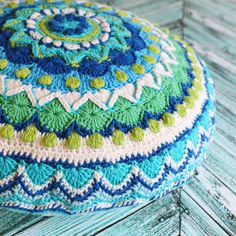 a crocheted blue and green poufle sitting on top of a wooden floor