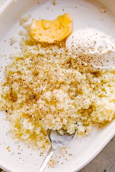 a white plate topped with mashed potatoes covered in seasoning next to a lemon wedge