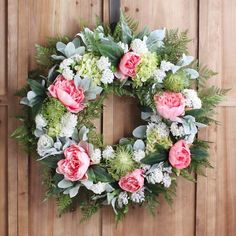 a wreath with pink and white flowers hanging on a wooden door