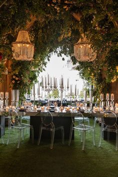 an outdoor dining area with clear chairs and greenery on the walls, surrounded by hanging chandeliers