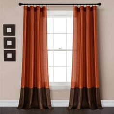 an orange and brown curtain hangs in front of a window with two black framed pictures on the wall