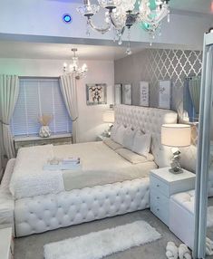 a white bed sitting in a bedroom next to a dresser and mirror with lights on it